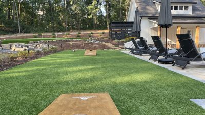 Synthetic turf backyard lawn with cornhole boards and modern outdoor lounge area